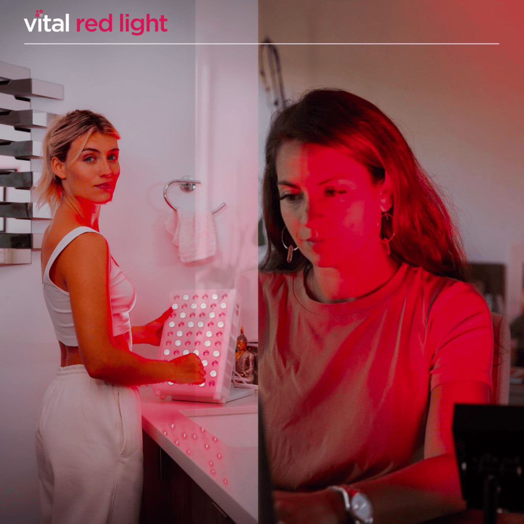 Two women are exposed to red light therapy indoors. One stands near a light panel, while the other uses a laptop. The scene is lit with a red glow.