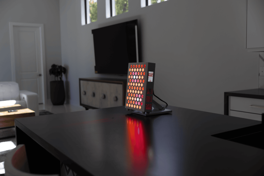 A Vital Pro 2.0 red light therapy panel is turned on and placed on a black kitchen counter in a modern, sunlit living space.