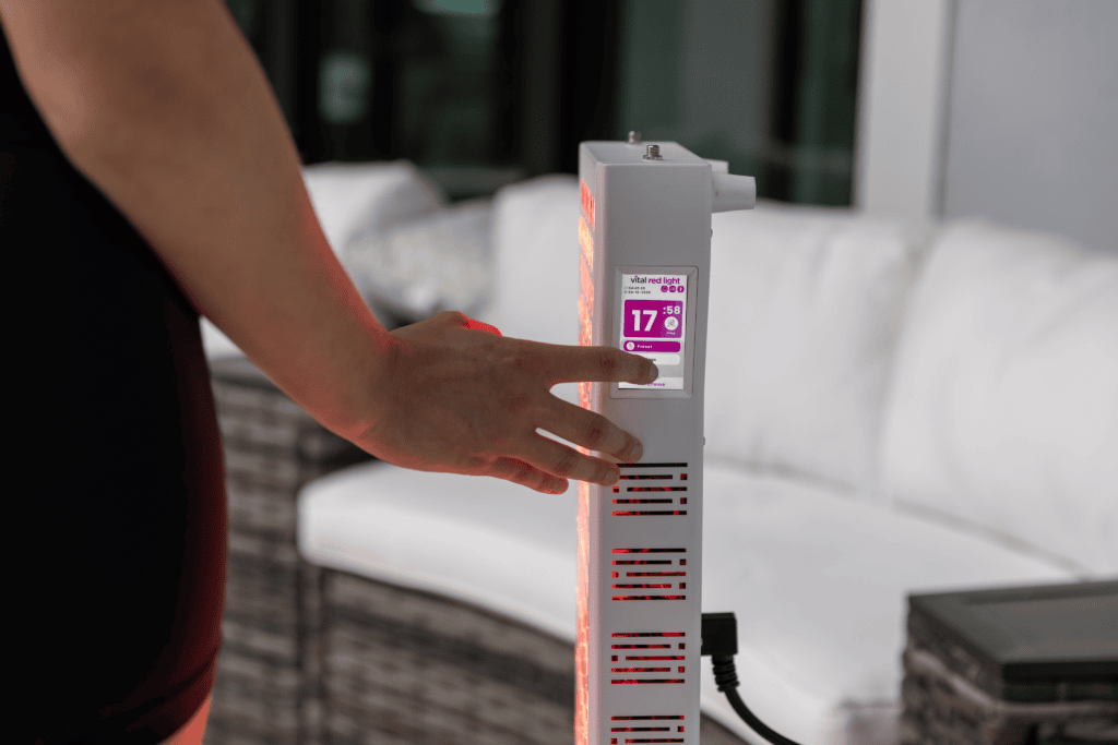 A person presses a button on the Vital Pro 2.0 electronic device with a digital display reading "17:00" near a white outdoor sofa set.